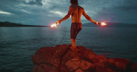 Strong athletic man walking on a sea cliff with burning red hot flares getting ready to jump into the sea, extreme cliff diving moments