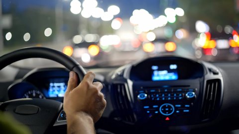 Man hands on steering wheel. Driving car in evening city through traffic jam