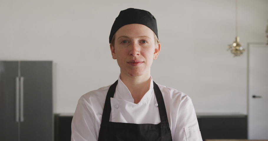 Portrait close up of a Caucasian female chef wearing chefs whites, a black hat and apron, standing in a cookery class, looking to camera and smiling, in slow motion Royalty-Free Stock Footage #1046711653