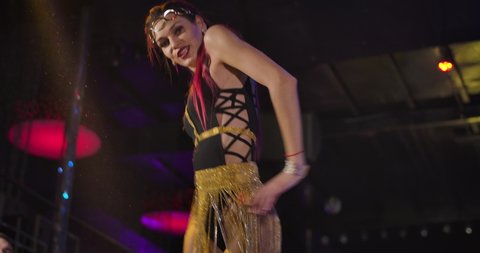 Camera moving up and down showing young female PJ with red hair and tattooed hand dancing on stage in night club. Beautiful seductive girl entertaining in disco. Cinema 4k ProRes HQ.