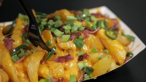 Slow Motion of fork in golden french fries with melted stretching cheddar cheese and sprinkled with fresh spring onions cooked crispy bacon and spicy jalapeño