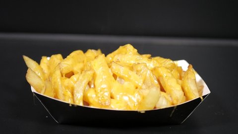 Slow motion top down shot of crispy golden hot steamy french fries with melted shredded cheddar cheese 