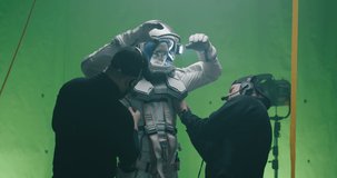 Medium shot of crew members helping an actor with a spacesuit costume and giving him drink