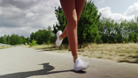 Closeup shot of woman running on asphalt road during summer