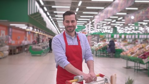 Portrait of happy smiling handsome middle aged seller man in supermarket with shopping cart positive millennial employee looking at camera, smiling face satisfied with good job successful people story