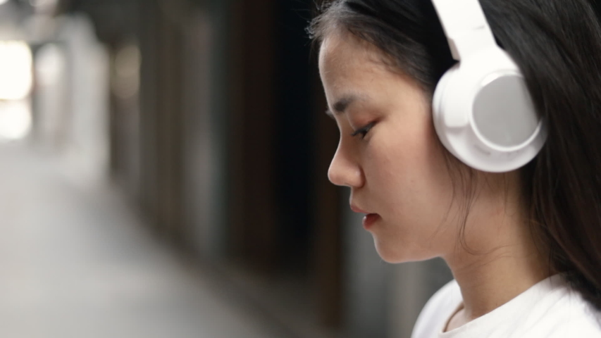 Attractive asian woman wears headphones listening to music and using smartphone checking social media communication with friends.