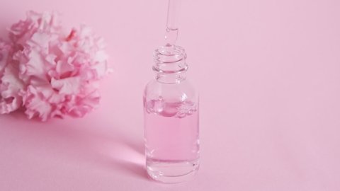 Dropper glass bottle with oil. Bottle with a cosmetic pipette. Antiaging moisturizing cosmetic product. Skin and body care. Pink oil essence flower product. Perfume.