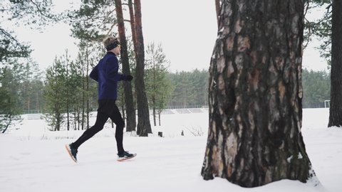 Running Man In Sportswear Workout Before Triathlon. Runner Man Running Winter Forest Snow Trail. Winter Sports And Recreation Concept. Frame on the clearance of trees
