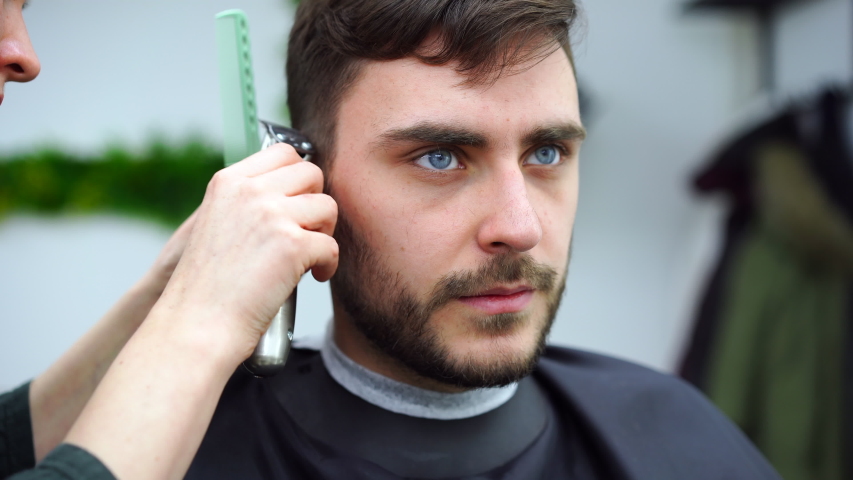 Stylish man sitting barber shop Hairstylist Hairdresser Woman cutting his hair Portrait handsome happy young bearded caucasian guy getting trendy haircut Attractive barber girl working serving client 