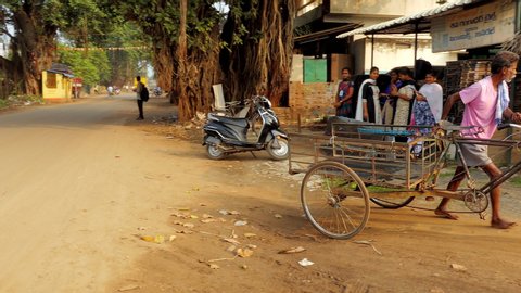 Yeleswaram , Andhra Pradesh / India - 11 02 2019: Barefooted Indian village man pushes three wheeled bicycle rickshaw cart purposefully off village road and up a side lane in Yeleswaram, Andhra Prades
