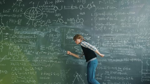 Funny young man student is dancing having fun near chalkboard with formulas enjoying successful education. People and positive emotions concept.