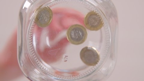 A worm's eye view of pound coins being dropped into a glass jar in slow motion