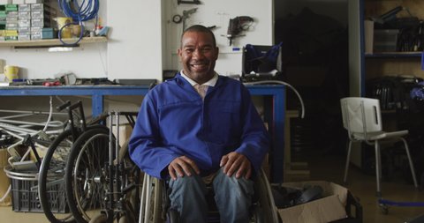 Portrait of an African American male worker in a workshop at a factory making wheelchairs, turning and looking to camera and smiling, sitting in a wheelchair