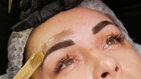 Correction of a beautiful aesthetic shape of eyebrows with hot wax and special tweezers. Removing unnecessary hair from the face