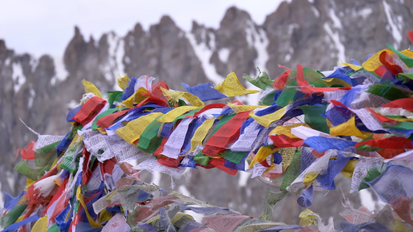 Slow motion shot of colourful Buddhist praying flags are waving with the wind next to a mountaintop monastery while Himalaya snow peaks are visible in the background.  