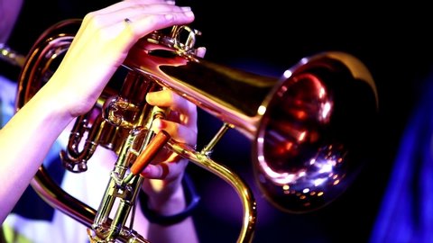 Close-up of a Golden flugelhorn in the hands of a trumpeter girl performing a solo concert.Fingers alternately press the valves of a brilliant wind instrument playing in a night club.Selective focus