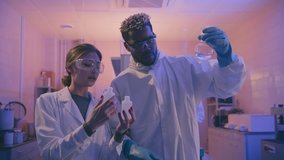 Young afro-american pharmacist studying chemicals in glass flask, his beautiful female colleague asking advice about reagents. Team of young scientists working on new vaccine in laboratory. - Powered by Shutterstock - Get 15% off with code: PIKWIZARD15