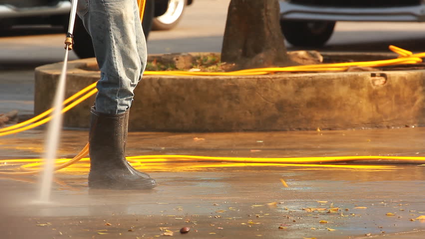 Worker cleaning with high-pressure cleaner water on ground