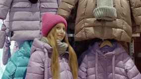 Teenager girl trying down jacket in clothes boutique at shopping. Happy young girl showing new down jacket in shopping store. Youth shopping in showroom