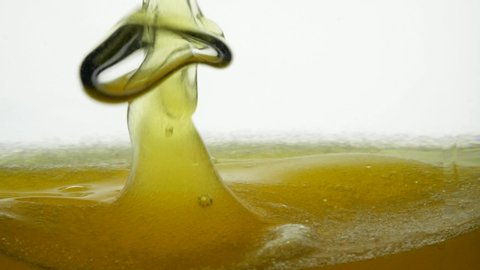 A close-up view of fragrant rapeseed and sunflower oil from which the air bubble is upright on a white background. Close shot of a golden liquid sediment. The surface of linseed oil in a container.