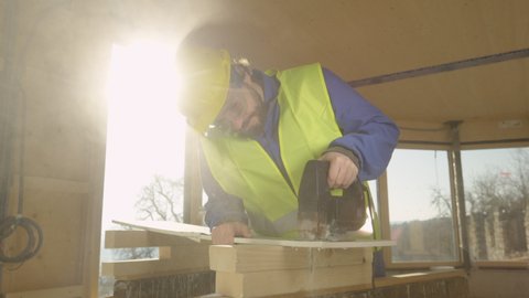 SLOW MOTION, LENS FLARE, CLOSE UP: Builder working in a CLT house cuts a gypsum wall panel with jigsaw. Caucasian worker building a contemporary solid wood house is trimming a thin plaster wall panel.