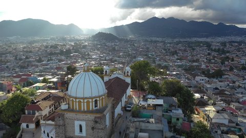 Aerial view of San Cristobal de las Casas in Chiapas, Mexico. Drone orbiting around the church in Mexico. Beautiful sunset over the city with sunrais striking through the clouds.