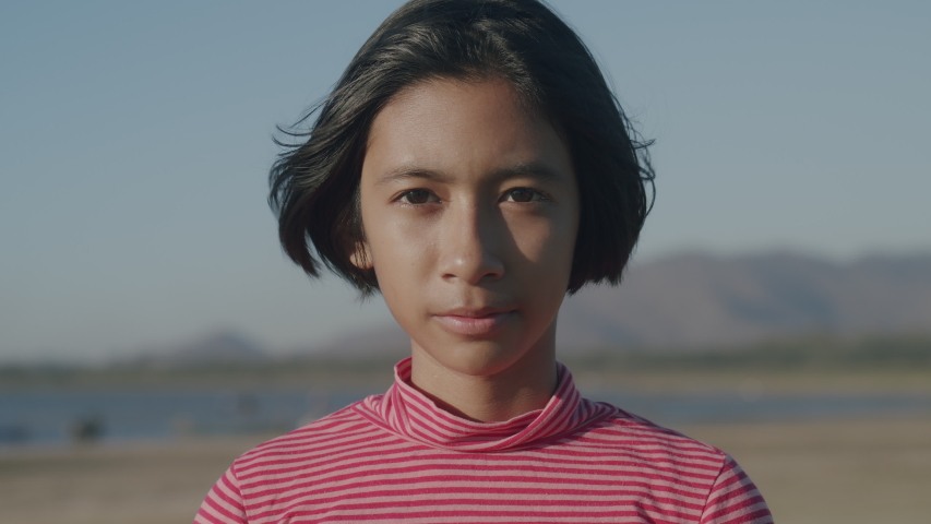 Medium close up of asian little girl smile and happy enjoying nature on beach at sunset. Close up of asia girl on face expression. relaxation lifestyle concept