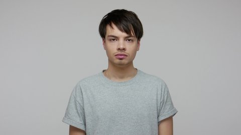Confused young man in T-shirt covering nose with hand, holding breath to avoid repulsive smell, disgusted by unpleasant intolerable odor, stink and fart. indoor studio shot isolated on gray background