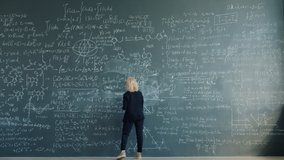 Time-lapse of female scientist blonde in elegant suit writing formulas on chalkboard working alone concentrated on theory. People and education concept. - Powered by Shutterstock - Get 15% off with code: PIKWIZARD15