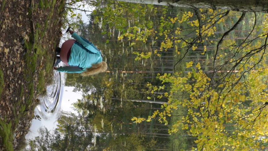A young woman draws water from a forest lake and makes coffee on an open fire. Two female friends enjoying the silence and fresh air. A vertically-oriented video.