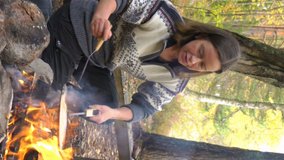 Female friends cooking traditional pancakes over an open fire in the camp outdoor, enjoying the silence and fresh air. A vertically-oriented video.