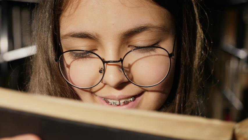 Girl with glasses reading a book in the library, extreme close-up, slow motion