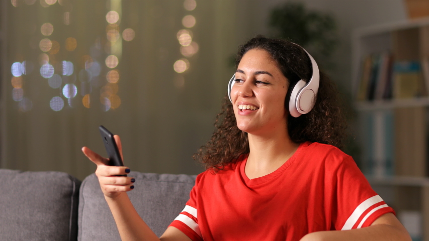 Happy arab girl dancing and listening to music with smart phone and headphones at home in the night Royalty-Free Stock Footage #1046817790