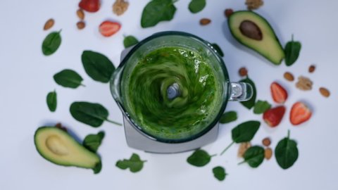 Healthy green smoothie blended with a blender. spinach and avocado on a white background top view. Close up of cooking in slow motion.