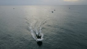 Early morning Tilt-down 4k aerial drone view following fisherman on a speed boat, leaving a white boat wake trail, on the dark blue Indian Ocean, Sri Lanka