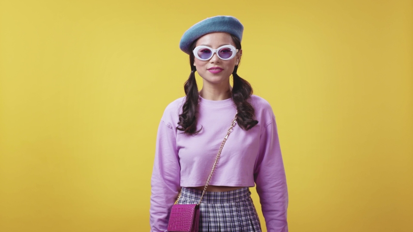 Nice-looking thai young woman wearing trendy fashion white sunglasses and posing happy at camera. Copyspace. Yellow background. Feelings and emotions.
