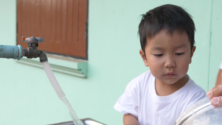 Asian little child boy helping grandmother wash pot with happy relaxing family time together. Kid learning to clean pot, doing housework. ef concept.