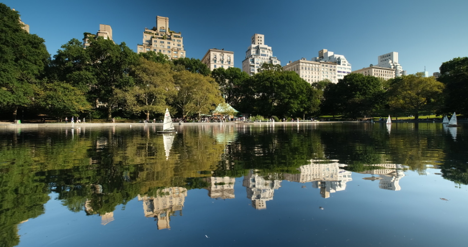 Luxury high end apartment and condominium residences rise up over the Conservatory Water and the Manhattan skyline in Central Park in New York City USA Royalty-Free Stock Footage #1046835754