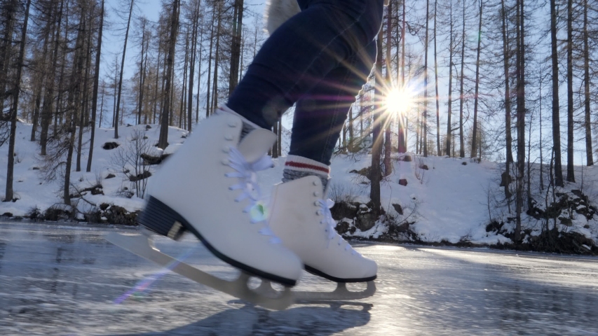 Close up on feet in ice skates on frozen lake. Sun rays passing trough pine wood forest on frozen lake. Woman ice skating in winter. 