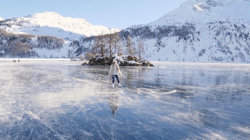 Young woman ice skating on frozen lake in winter. Female on ice skates surrounded by stunning mountain landscape. Natural frozen lake in the Alps. Woman enjoying winter season 