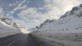 Car point of view driving on road in winter, snowy mountains all around. Swiss Alps, Switzerland. vehicle driving in ski season on road through nature on sunny day. pov car road trip 4K video