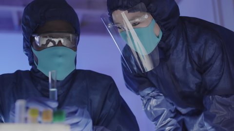 Close up of male African researcher wearing coverall and his female Asian assistant looking at liquid in glass tube and nodding