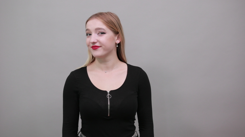 Young blonde girl in black jacket on grey background happy woman smiles and points the direction with her index finger, demonstrates something