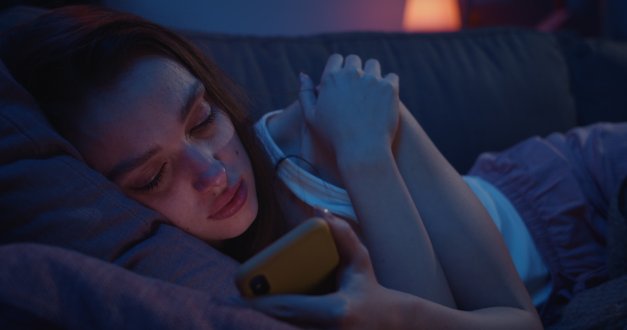 Close up of lonely young woman lying on sofa and using smartphone at night. Depressed millennial female starring at mobile phone screen and thinking. Concept of painful brokeup. Royalty-Free Stock Footage #1046847817