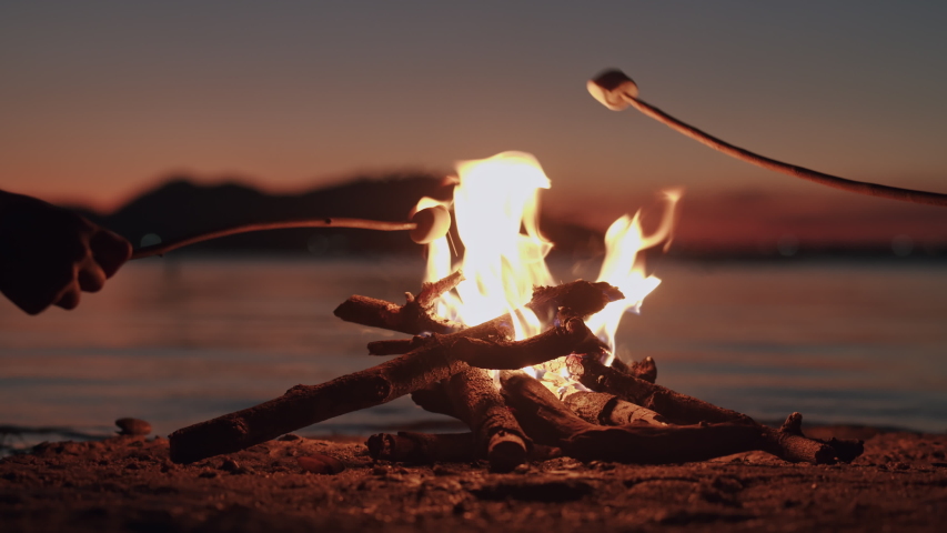 Hand of asian family  with marshmallow on a stick being roasted  over a camping  fire at  night, Campfire on the beach and the wind on the water surface. The concept of family lifestyle on holiday Royalty-Free Stock Footage #1046849542