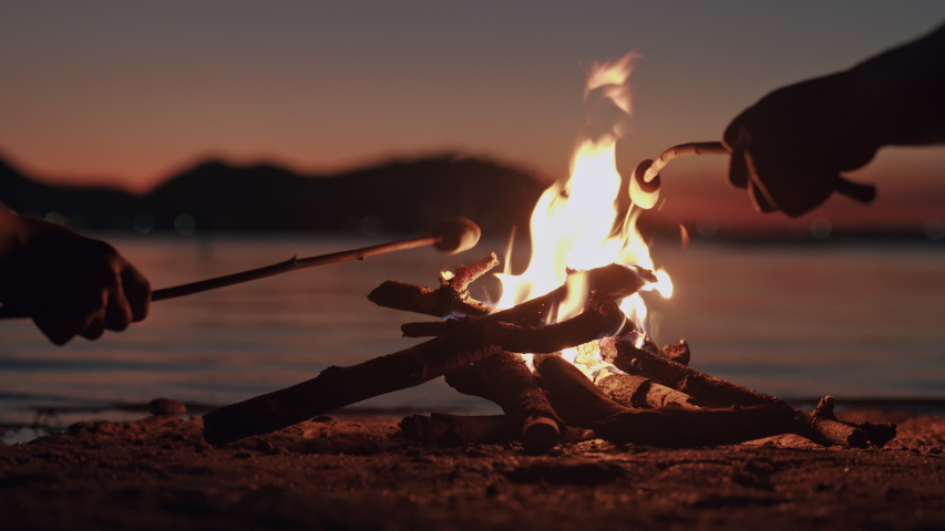 Hand of asian family  with marshmallow on a stick being roasted  over a camping  fire at  night, Campfire on the beach and the wind on the water surface. The concept of family lifestyle on holiday | Shutterstock HD Video #1046849542