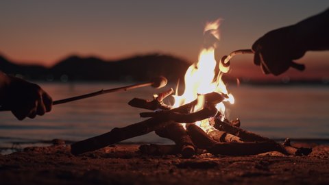 Hand of asian family  with marshmallow on a stick being roasted  over a camping  fire at  night, Campfire on the beach and the wind on the water surface. The concept of family lifestyle on holiday