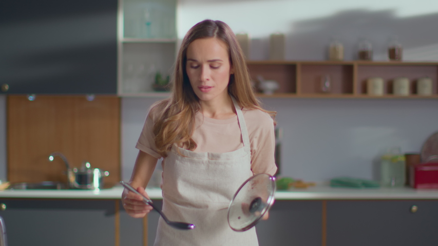 Pretty woman cooking soup on stove at kitchen. Close up of housewife preparing dinner at home. Young woman tasting soup on spoon at modern kitchen in slow motion | Shutterstock HD Video #1046849713