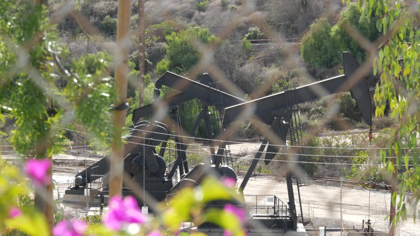 Industrial urban landscape. La Brea Inglewood in Los Angeles. Well pump jack operating behind the fence. Drilling rig extract crude oil. Oil mining machine with working piston. Oil and gas industry.