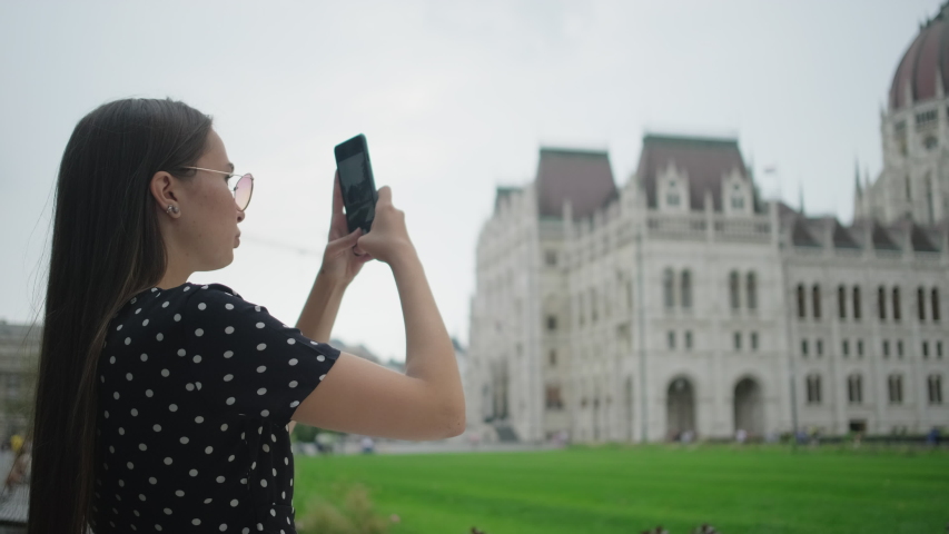 Girl tourist with smartphone shooting Hungarian Parliament Building in Budapest. She wants to add photos to her collection of visited places